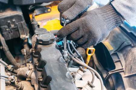 Mechanic's hands unscrew the valve cover of an internal combustion engine to replace the gasket.