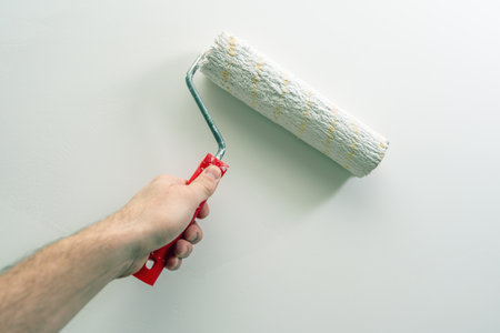 A man's hand paints a wall white with a paint roller.の写真素材