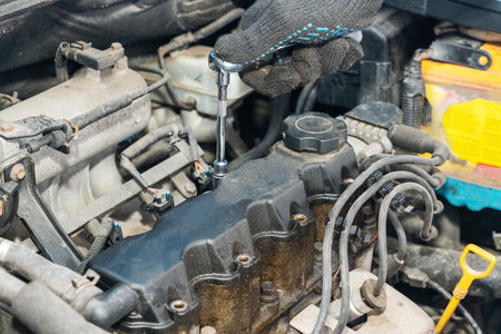 Mechanic's hands unscrew the valve cover of an internal combustion engine to replace the gasket.