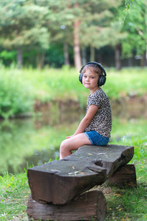 Cute little girl in modern wireless headphones enjoys music outdoors.の写真素材