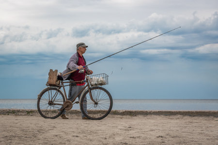 Skadovsk, Ukraine, June 06, 2021: An elderly man with a fishing rod leads an old bicycle along the seashore.のeditorial素材