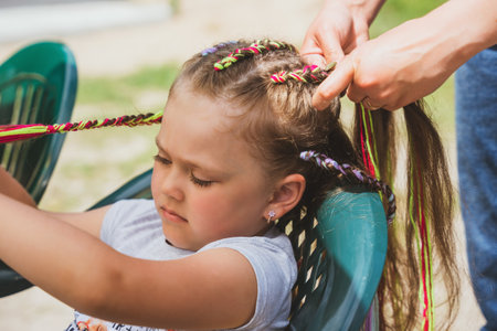 Girl hairdresser braids colorful ropes into little girl's hair.の写真素材