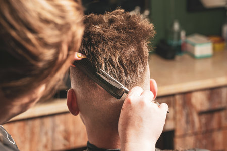 Girl hairdresser doing hairstyle and styling with scissors and comb to a young man.の写真素材