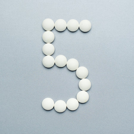 The number 5 made of white pills on a gray background.