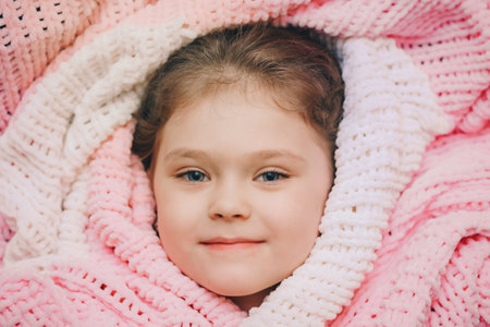 Cute beautiful smiling little girl lying on her back wrapped in a blanket.の写真素材
