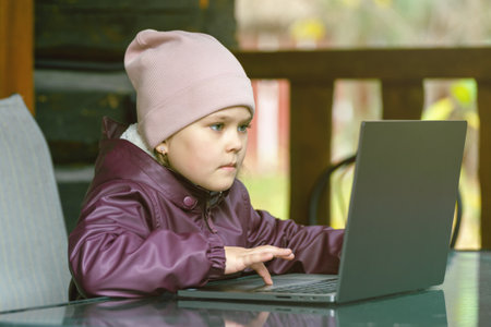 Cute little girl using a laptop computer for online learning or communication sits on a terrace in a country house.の写真素材