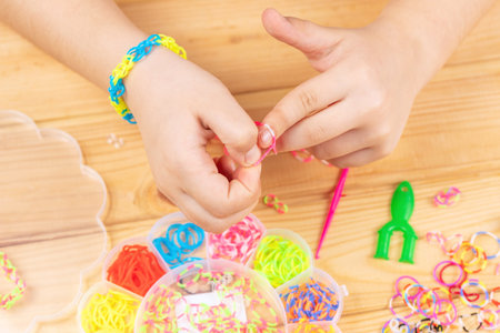 Hands of a girl weaving a bracelet with multi-colored rubber bands. Development of fine motor skills of fingers.の写真素材