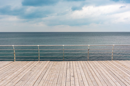 Empty seaside promenade with wooden decking and metal handrails on a cloudy day.の写真素材