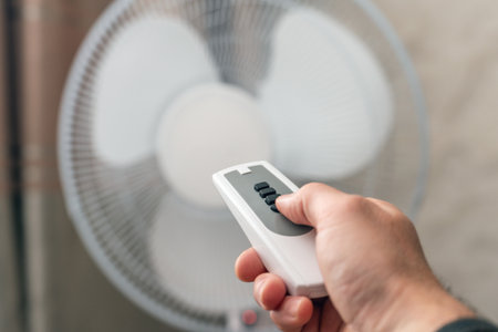 Man using remote control to turn on or off floor fan in room.の写真素材