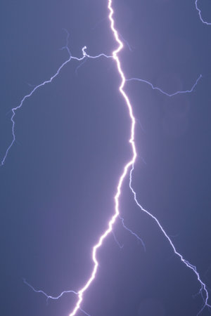 Powerful lightning bolt illuminating dark stormy night sky with dramatic clouds.