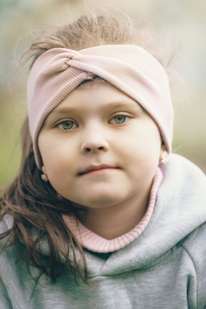 A Portrait of a Young Girl Wearing a Soft Pink Headband with Gentle Expressions, Showcasing Facial Features and a Natural, Outdoor Settingの写真素材