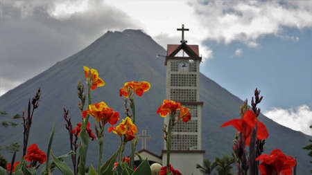 The Arenal volcano with the belfry and bright flowers in the foregroundの写真素材
