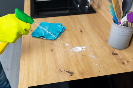 Cleaning the kitchen table with a rag and a sprayer.