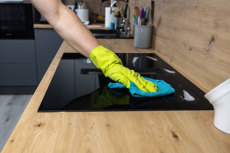cropped image of woman in rubber gloves cleaning induction hob in kitchen