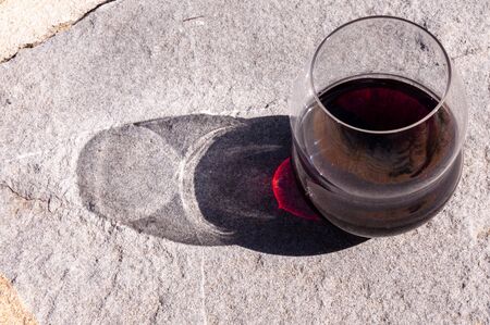 A glass of red wine with a bright shadow is on a stone surface.の写真素材