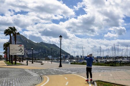A boy stands on the road and photographs the rock of Gibraltar against the backdrop of the marina...