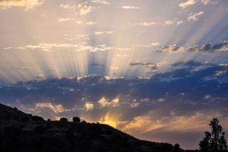 Sunrise over the horizon with bright contrasting rays illuminates the sky with cloudsの写真素材