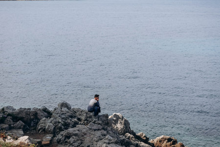 Antibes, France - 20 May 2023: A man sitting on a rocky shore near Antibes, on the French Riviera