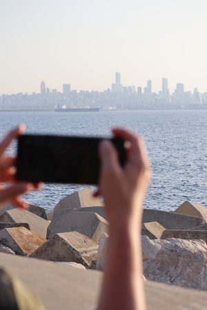 Hands holding a smartphone and photographing the skyline of Beirut, Lebanon. Unfocused on purposeの写真素材