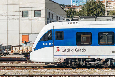 Trieste, Italy - August 18, 2024: A blue and white ETR 563 train, labeled CittÃ  di Grado, moves...
