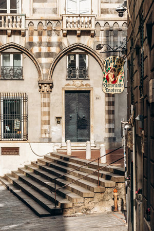 Genoa, Italy - September 22, 2024: Vintage Migone Ristorante Enoteca sign hangs beside striped medieval arches and stone steps in Piazza San Matteo.のeditorial素材