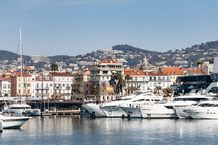 Cannes, France - March 8, 2025: Fishing boats and yachts in the Old Port with Palais des Festivals and city hills in the background.の写真素材