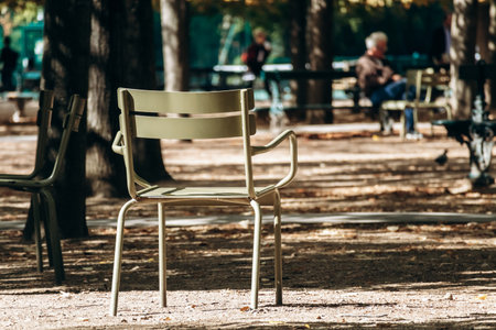 Iconic green metal chairs stand empty on a sunlit gravel path in the famous city park - Luxembourg Garden, Paris, Franceの写真素材