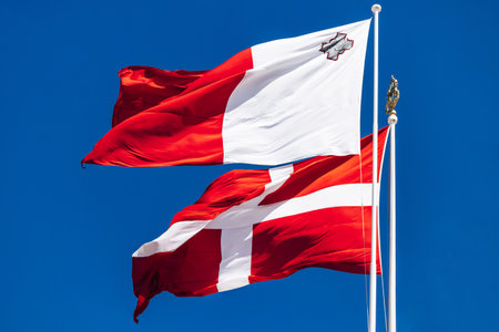 The national flag of Malta and the flag of the Sovereign Military Order of Malta waving on flagpoles against a clear blue sky.の写真素材