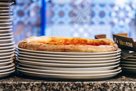 Fresh pizza resting on stacked white plates at restaurant counterの写真素材