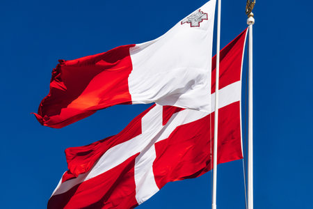 The national flag of Malta and the flag of the Sovereign Military Order of Malta waving on flagpoles against a clear blue sky.の写真素材