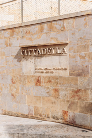 Closeup of the âCITTADELLAâ stone sign at the main entrance to the Cittadella Visitors Centre, set into a limestone wall in bright sunlight, marking the gateway to Gozoâs historic fortress in Victoriaの写真素材
