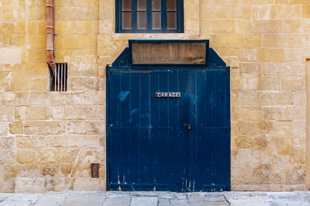 Classic navy blue wooden garage door with metal sign CARACE in white letters set into a traditional Maltese limestone facade in the historic city center of Vallettaの写真素材