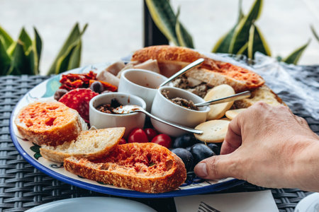 A traditional Maltese wine tasting platter with local appetizers, including tomato bruschetta, olives, pÃ¢tÃ©s, cherry tomatoes, cold cuts, and bread, served on a decorative ceramic plateの写真素材