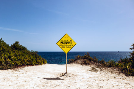 Bright yellow warning sign reading â€œFalling Rocks â€“ Danger High Risk Area Keep...