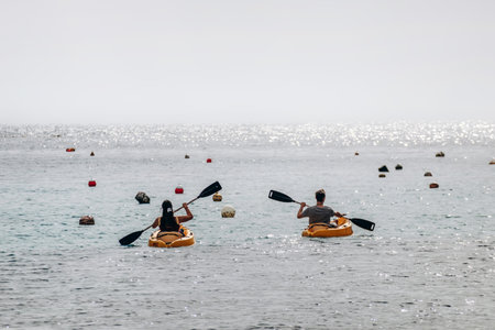 Xlendi, Gozo, Malta - April 12, 2025: Two people kayaking on calm shimmering water among floating buoys under the afternoon sunのeditorial素材