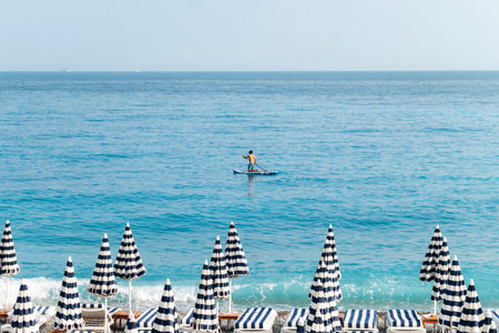 Man paddleboarding near the beach with striped umbrellas in Nice, on the French Rivieraの写真素材