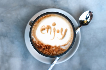 Close-up of latte coffee in a transparent cup with "Enjoy" written on the milk frothの写真素材