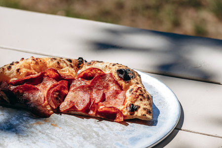 A rustic pepperoni pizza slice with a thick, airy crust, photographed outdoors in natural sunlight...