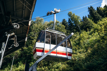 Chambord, Canada - August 18, 2025: White and red aerial tram car hanging from cables against forest at Val-Jalbert Historical Village in Quebecのeditorial素材