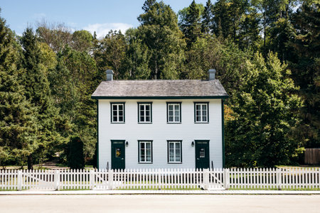 Chambord, Canada - August 18, 2025: Restored white two-story house with green trim and picket fence at Val-Jalbert Historical Village in Quebecのeditorial素材