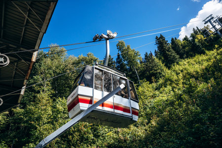 Chambord, Canada - August 18, 2025: White and red aerial tram car hanging from cables against forest at Val-Jalbert Historical Village in Quebecのeditorial素材