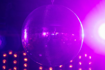 Close-up of a spinning disco ball illuminated by pink, purple, and blue lights inside a nightclub.