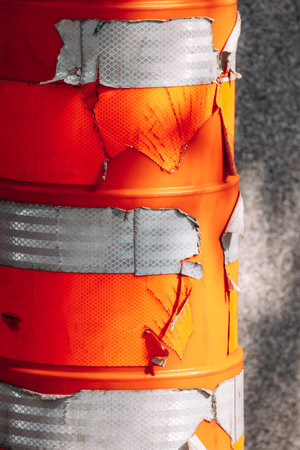 Close-up view of damaged orange traffic construction barrels with peeling reflective tape in downtown Montreal, showing urban wear, texture, and details of roadwork equipment.の写真素材