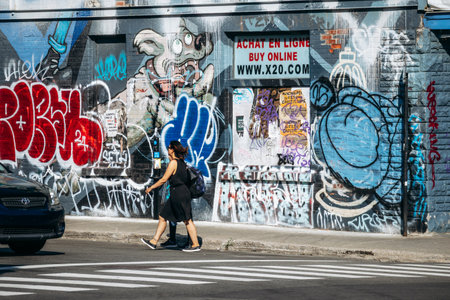 Montreal, Canada - August 12, 2025: Diverse people crossing urban street at graffiti mural, downtown summer dayのeditorial素材