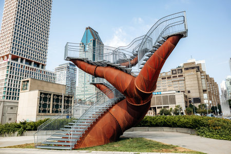 Montreal, Canada â August 14, 2025: A striking public art installation with large rust-colored steel structures and elevated walkways set against the modern downtown skyline of Montrealのeditorial素材