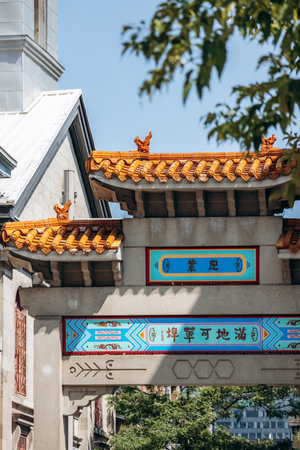 Montreal, Canada - August 14, 2025: Traditional Chinese gate in the heart of Montreal Chinatown, featuring ornate orange roof tiles, decorative mythical figures, and colorful painted inscriptions.のeditorial素材