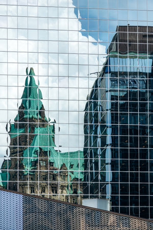 Ottawa, Canada - August 13, 2025: Reflection of the historic Confederation Building in the glass facade of a modern office tower in downtown Ottawaのeditorial素材