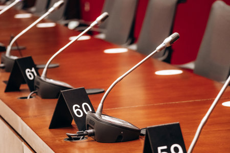 Ottawa, Canada - August 13, 2025: Modern Senate of Canada committee room with long wooden tables, microphones, grey chairs, and two Canadian flags in a conference setup.のeditorial素材
