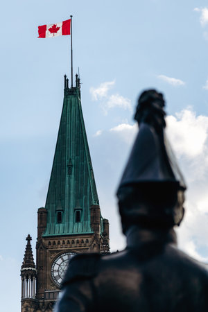 Ottawa, Canada - August 13, 2025: Out of focus statue of Lieutenant Colonel John By in the foreground with the clock tower and Canadian flag of the Parliament of Canada sharply visibleのeditorial素材