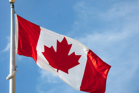 Canadian flag waving on a tall metal flagpole against a clear blue sky in downtown Ottawa.